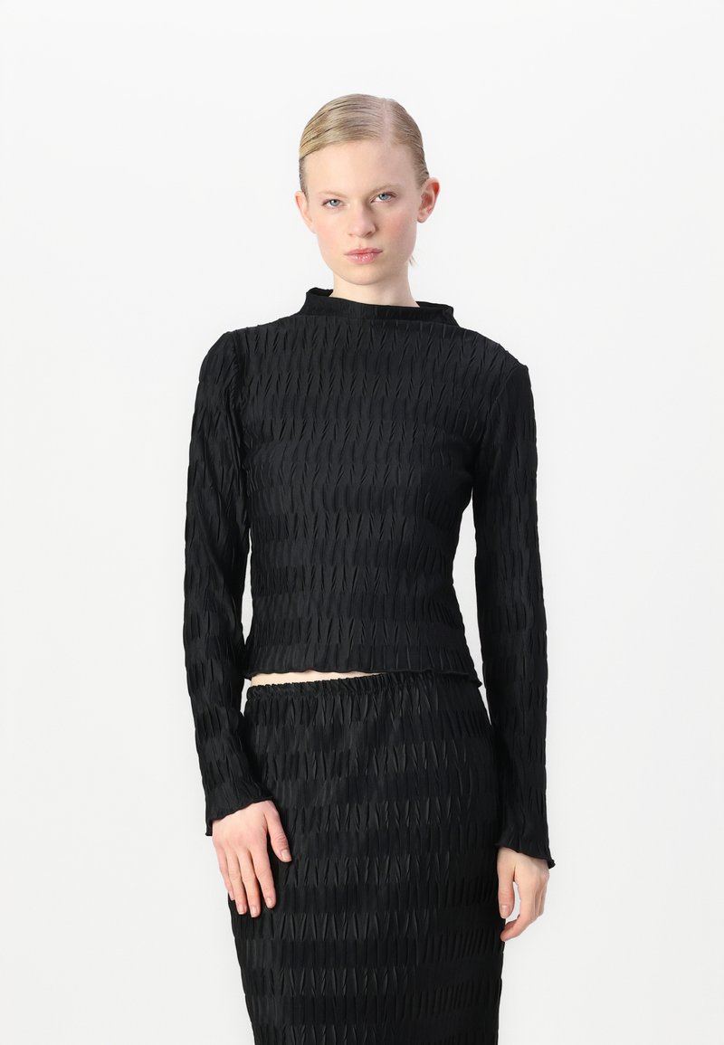 Juodas tekstūruotas ilgomis rankovėmis viršus su aukštu kaklu, apdaras su raštuota medžiaga ir slim fit siluetu, derinamas su atitinkama sijonu.