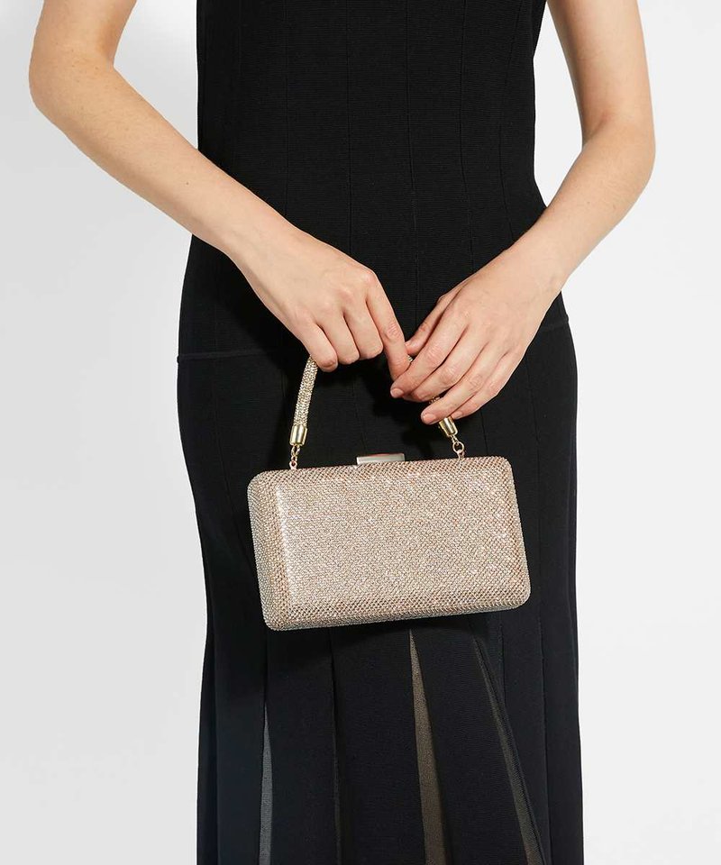 Mains tenant une petite pochette rectangulaire scintillante avec une courte anse, portée avec une robe noire cintrée.