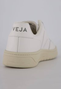 Hvide lædersneakers med off-white sål, der har en struktureret overflade. "VEJA" logo i grå på hælen, minimalistisk design med syninger.