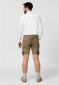 Braune Lederhosen mit abgenutzter Struktur, seitlichen blauen Akzenten und einem klassischen Schnitt. Kombiniert mit einem weißen Hemd und grauen Schuhen.