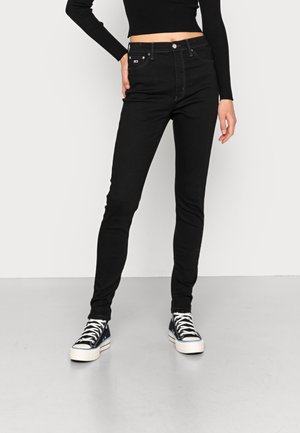 Jeans negros ajustados de cintura alta, con un diseño clásico de cinco bolsillos, detalles de costura sutiles y combinados con zapatillas negras.