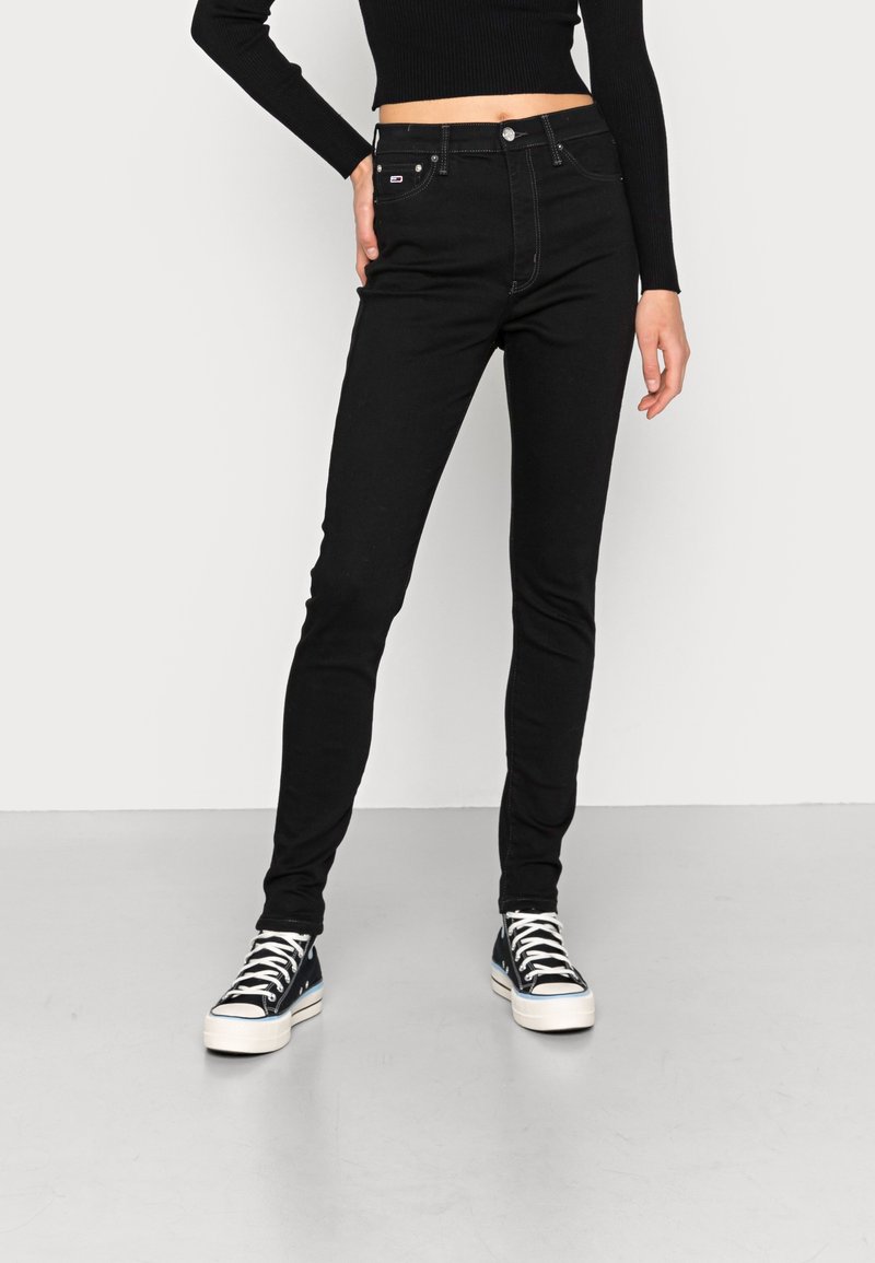 Jeans negros ajustados de cintura alta, con un diseño clásico de cinco bolsillos, detalles de costura sutiles y combinados con zapatillas negras.