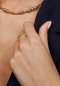 Gul pärlband och matchande ring med glänsande, runda pärlor. Närbilden visar en hand som vilar på kläder, som visar släta texturer.