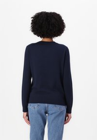 Granatowy sweter z długimi rękawami, okrągłym dekoltem i ściągaczami na mankietach. Połączony z jasnoniebieskimi dżinsami o standardowym kroju i minimalnym zdobieniu.