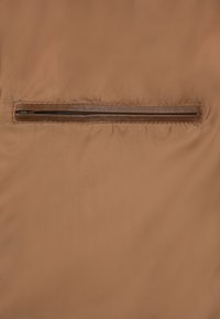 Brun jakke med en glat tekstur, der har en vandret lynlås lomme i en mørkere brun farve i midten. Subtil glans på stoffet.