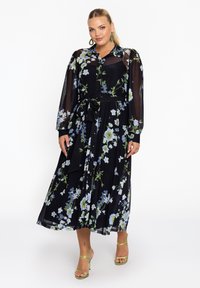 Schwarzes Blumenkleid mit langen, durchsichtigen Ärmeln, knöpfbarem Vorderteil und gebundenem Taillengürtel. Verfügt über blaue und weiße Blumen mit grünen Akzenten.