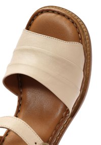 Sandali in pelle beige con cinturini larghi, una texture liscia e un sottopiede imbottito marrone. Dettagli cuciti e forma arrotondata.