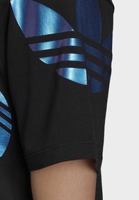 Svart t-shirt med en stor blå och teal grafisk logotyp på axeln, med en slät, glänsande yta och kontrasterande matt bakgrund.