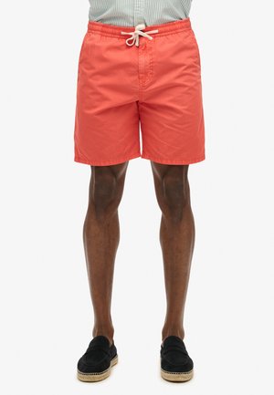 Maillots de bain corail en tissu léger, dotés d'une taille élastique avec un cordon blanc et des poches latérales.