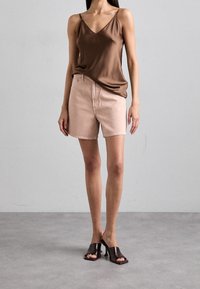 Top de camisón de satén marrón, pantalones cortos de mezclilla rosa claro y tacones abiertos marrones. Textura suave, diseño de escote en V y ajuste casual.