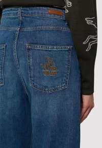 Blå denimjeans med en bakficka med en broderad Trussardi-logotyp, en läderetikett och en klassisk femficksdesign.