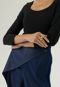 Zwarte langemouwen top gecombineerd met donkerblauwe asymmetrische broek, met een zwarte knopendetail en een gladde, gestructureerde stof. Gouden ringaccessoire.