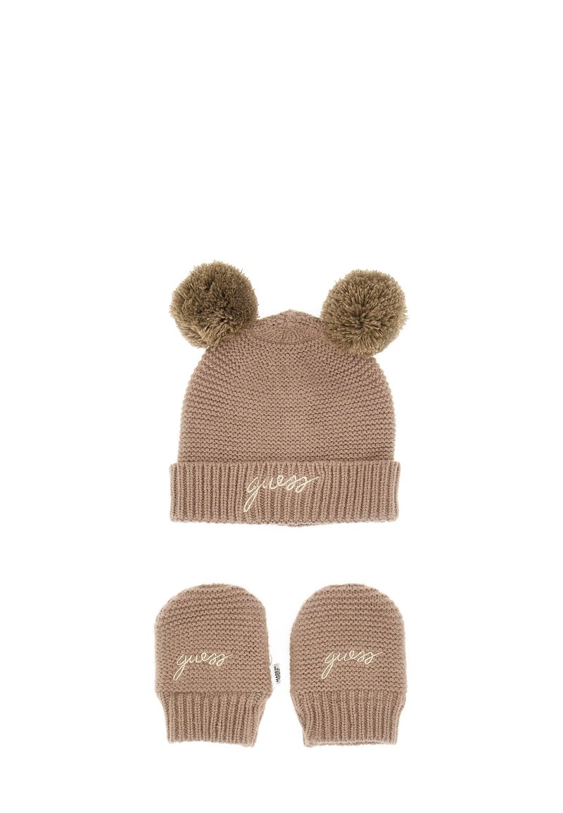 Tan gebreide muts met twee pompons bovenaan, met een geribde manchet en geborduurd "guess" logo. Een paar bijpassende vingerloze handschoenen eronder.