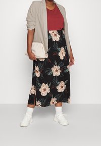 Gonna nera floreale con accenti beige e verdi, abbinata a una maglietta color bordeaux e a un blazer grigio chiaro. Borsa neutra e sneakers bianche completano il look.