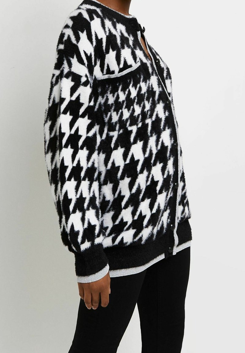 Svart och vit hundtooth-mönstrad cardigan med en fluffig textur, knappstängning och kontrasterande grå kant längs kanterna och kragen.