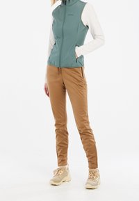 Lekki turkusowy kamizelka z wysokim kołnierzem, zestawiona z beżowymi elastycznymi joggerami. Sneakersy w jasnym beżu. Minimalistyczny design, bez widocznych wzorów.