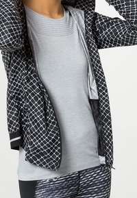 Person wearing a black and white patterned jacket over a light gray fitted shirt and black-and-white printed leggings.