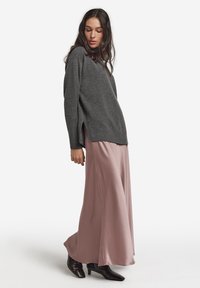 Grå strikket sweater med sideslidser kombineret med en lang, blød lyserød satinskørt. Sorte ankelstøvler med hæl fuldender outfittet.