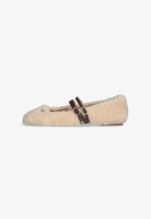 Chaussure plate beige en peluche avec deux sangles à boucle ajustables brun foncé sur le dessus et un petit emblème doré près du pied.