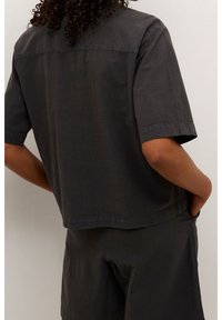 Sort bomuldsskjorte med korte ærmer, afslappet pasform, buet kant og subtil tekstur. Har en søm over ryggen og sidelommer.