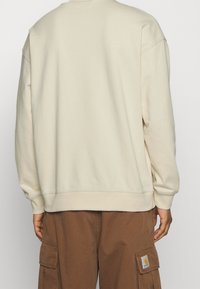 Krémová mikina s kulatým výstřihem, ribovanými manžetami a volným střihem. Nosit s hnědými cargo kalhotami s náprsní kapsou.