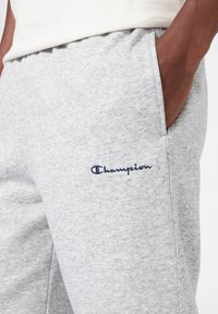 Pantaloni sportivi in cotone grigio con vita elastica, tasche laterali e logo "Champion" ricamato in blu navy sulla coscia.