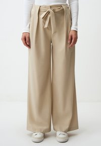 Beige wijde broek met een gestrikte tailleband, met een gladde textuur en een vloeiende uitstraling. GDRD in combinatie met witte sneakers.
