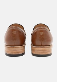 Braune Leder Schuhe mit strukturierter Oberfläche, ausgestattet mit einem niedrigen Holzabsatz und einer schwarzen Gummisohle. Abgerundetes Design mit subtilen Logodetails.