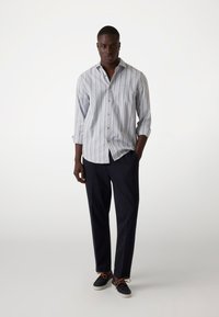 Heren overhemd met knopen, lichtblauw met witte strepen, lange mouwen. Gecombineerd met een donkere broek en casual schoenen, met bruine veters.