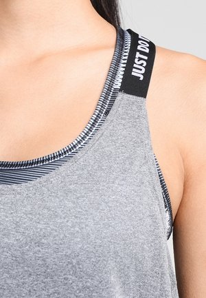 Primer plano de una persona que lleva una camiseta sin mangas gris sobre un sujetador deportivo a rayas en blanco y negro con el texto «JUST DO IT» en la tira del sujetador.