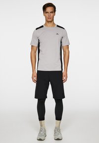 Grå atletisk t-shirt med svarta sidopaneler, kombinerad med svarta shorts och svarta leggings. Har en logo på den övre vänstra bröstet.