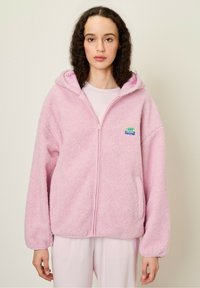 Svetloružová fleecová mikina s kapucňou, na zips, prednými vreckami a farebným logom značky na hrudi. Obsahuje kapucňu a elastické manžety na rukávoch.