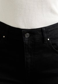 Black denim jeans feature a classic design with a front button closure and silver hardware. The fabric has a smooth, textured finish.