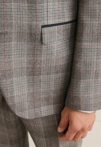 Giacca da suit grigia a quadri con piccoli motivi a scacchi neri e rossi, taschino sul petto singolo con rivestimento nero, tessuto testurizzato, vestibilità slim.