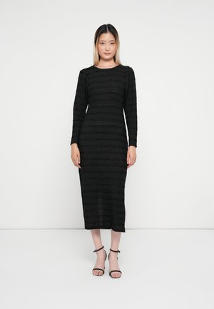 Robe noire à manches longues avec un motif rayé texturé. Longueur mi-mollet, dotée d'un col rond et d'une coupe cintrée. Sandales à talons noires.