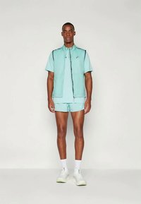 Myntgrønn treningstøy med en glidelåsvest, t-skjorte med kort erm og shorts. Inkluderer reflekterende detaljer og lett stoff.