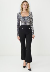 Beżowy body z długim rękawem w czarne wzory leopardzie, zestawione z czarnymi spodniami z wysokim stanem i rozszerzanymi nogawkami, zdobionymi złotymi guzikami.