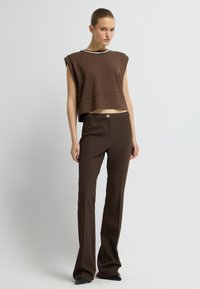 Bruine cropped trui met een halssnoer van parels, gecombineerd met bruin high-waisted broeken met een knoopsluiting en uitlopende broekspijpen.