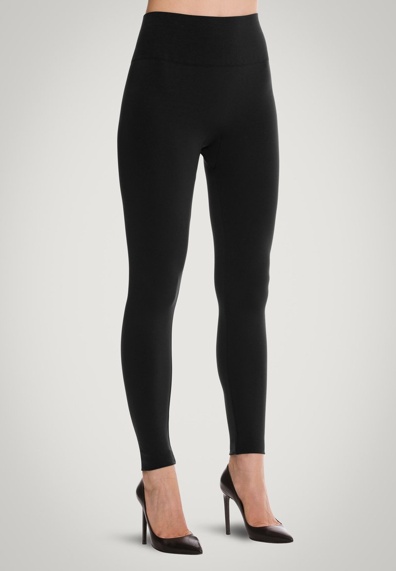 Leggings neri con vita alta, tessuto liscio e vestibilità elastica, abbinati a décolleté a punta.