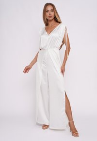 Weißer Satin-Jumpsuit mit V-Ausschnitt, kurzen Ärmeln mit Bindebändern und einem Schlitz vorne. Fließende Silhouette und weiter Beinschnitt für Bewegungsfreiheit.