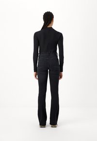 Black long-sleeve top with a high neck, paired with dark denim flared pants. The pants feature back pockets and a fitted waist.