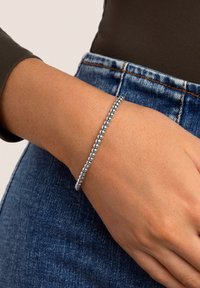 Handgelenk, das ein silbernes Perlenarmband trägt, kombiniert mit blauen Denim-Jeans und einem dunklen Langarmshirt.