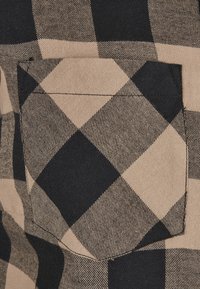 Tissu de chemise à carreaux noir et beige avec une poche carrée. Le matériau est en coton tissé avec un motif à carreaux.