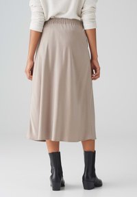Beige Midi-Rock mit einem gerafften Taillenbund, glatter Textur und fließendem Design. Kombiniert mit schwarzen Knöchelstiefeln für den Kontrast.