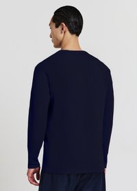Chemise à manches longues bleu marine en tissu texturé, avec un col rond, au design simple et épuré, et une coupe légèrement décontractée.