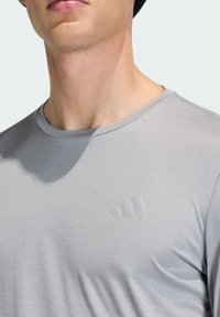 Light gray short-sleeve t-shirt with a subtle striped texture and a raised logo on the chest. Round neckline and relaxed fit.