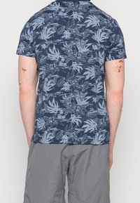 Navy blue T-shirt with short sleeves, featuring a floral pattern in light blue. Made of cotton, it has a relaxed fit and rounded hem.