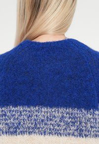 Wollpullover in kräftigem Blau mit strukturierter Oberfläche, der ein Gradientemuster aufweist, das am Saum zu hellblau und Creme übergeht.