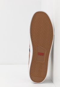 Brązowo-biały sneaker z gumową podeszwą o wzorze jodełki, na której widnieje czerwone logo "Levi's".