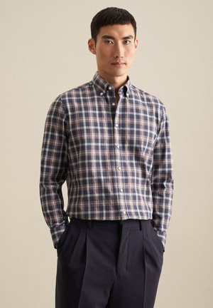 Overhemd met knoopsluiting in een blauw, bruin en crème ruitpatroon. Lange mouwen, kraag en een soepele stof. Gepaard met donkere broeken.